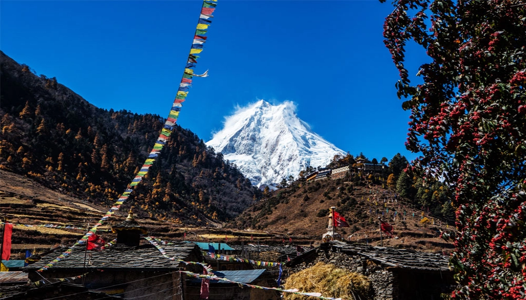 A prayer flag is fluttering on the roof of a house in Lo-gaun and Mount Manaslu in the background.